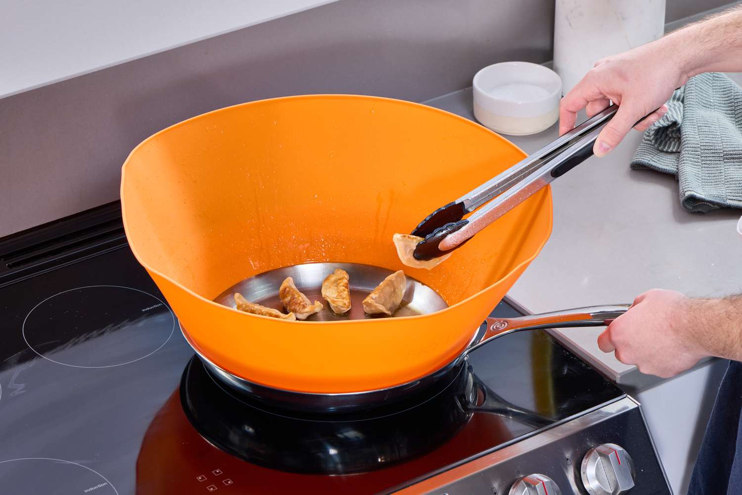 a person searing dumplings with a large orange splatter screen shaped like a funnel