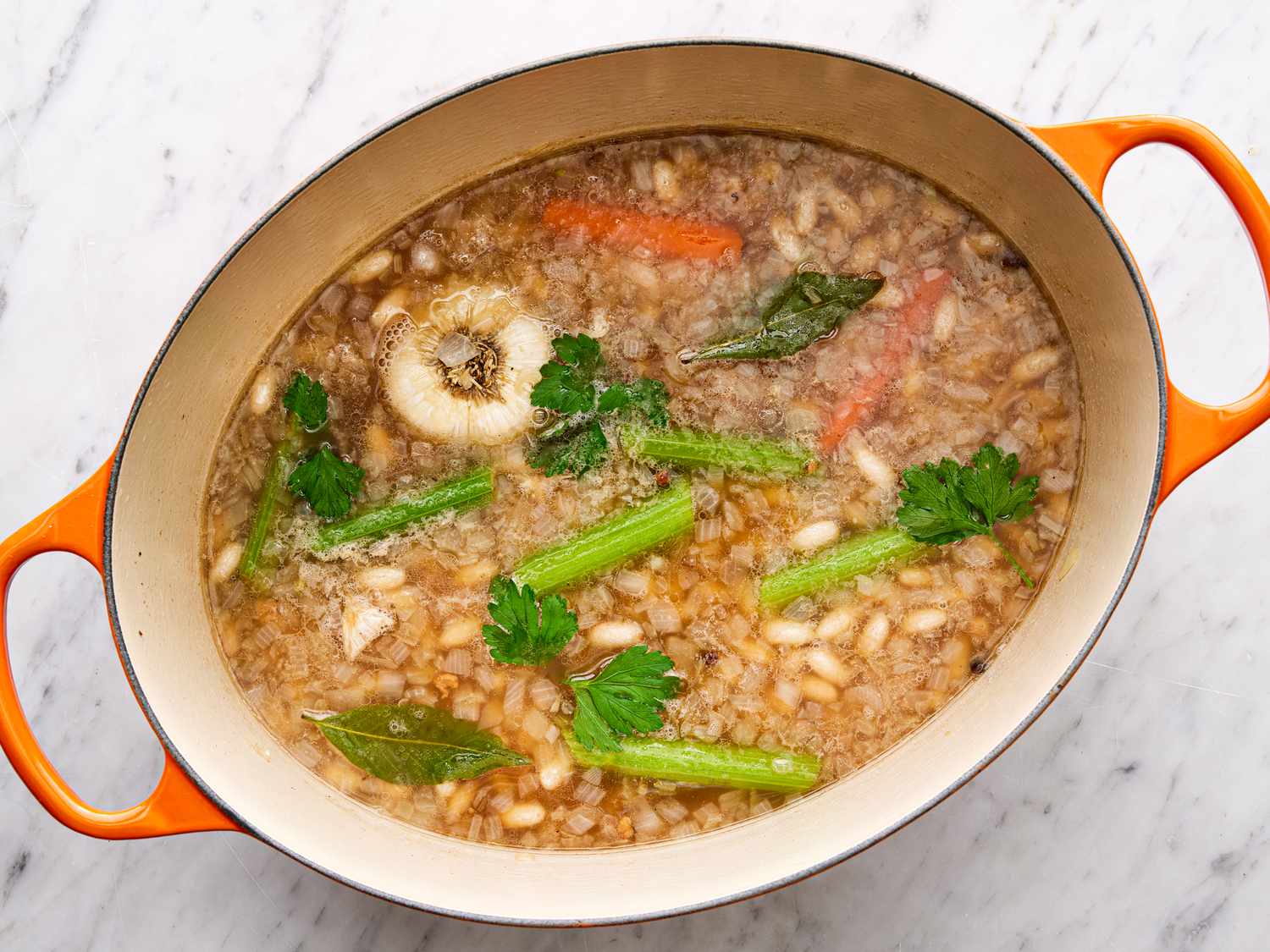 Overhead view of carrots, onion, celery, and beans added to pot