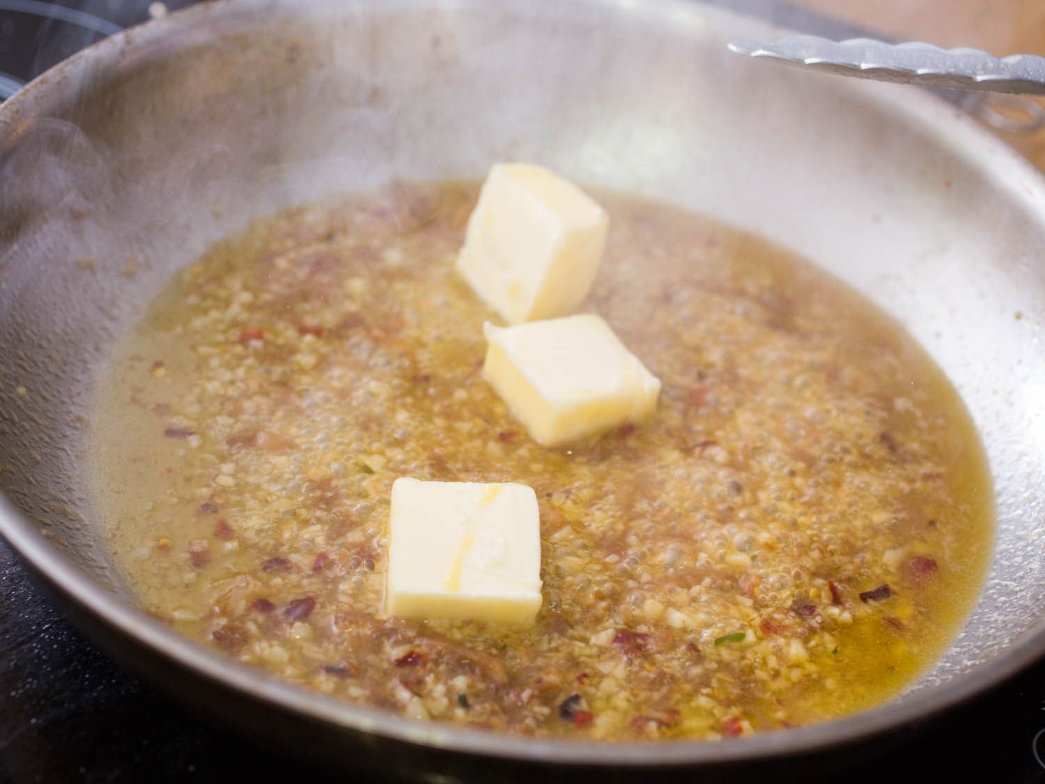 Three butter pats melting into reduced vermouth, olive oil, and garlic. in skillet.