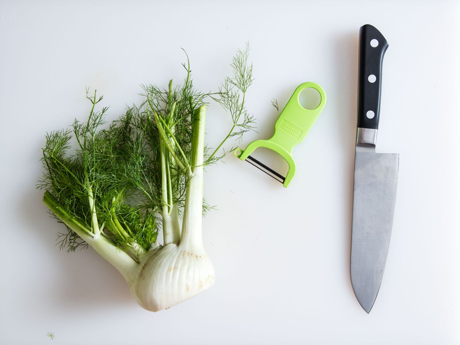 Fennel on a cutting board with a peeler and a chef's knife.