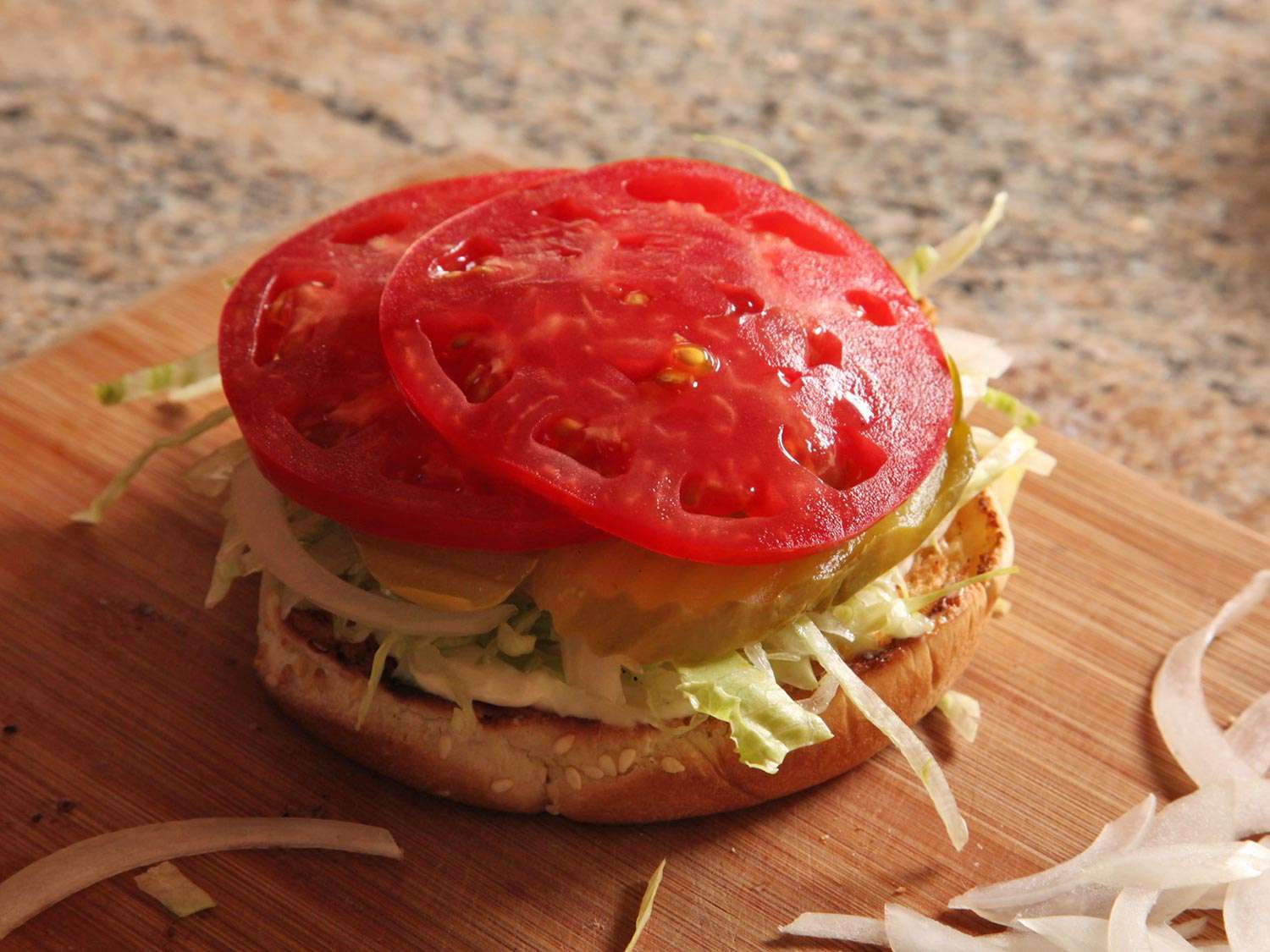 A bottom bun with all toppings/bottomings layered on, ready to receive a burger patty.