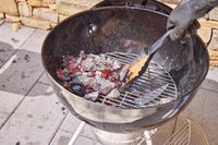 A gloved hand moving hot coals in the Weber Original Kettle Premium 22-Inch Charcoal Grill