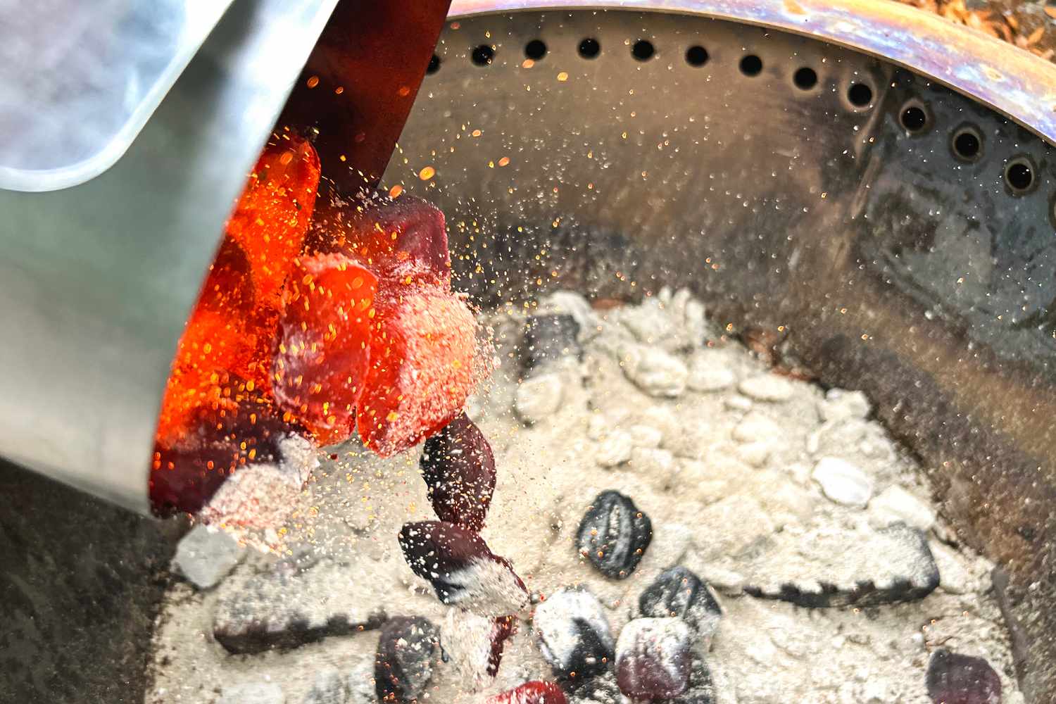 pouring hot coals into a charcoal grill