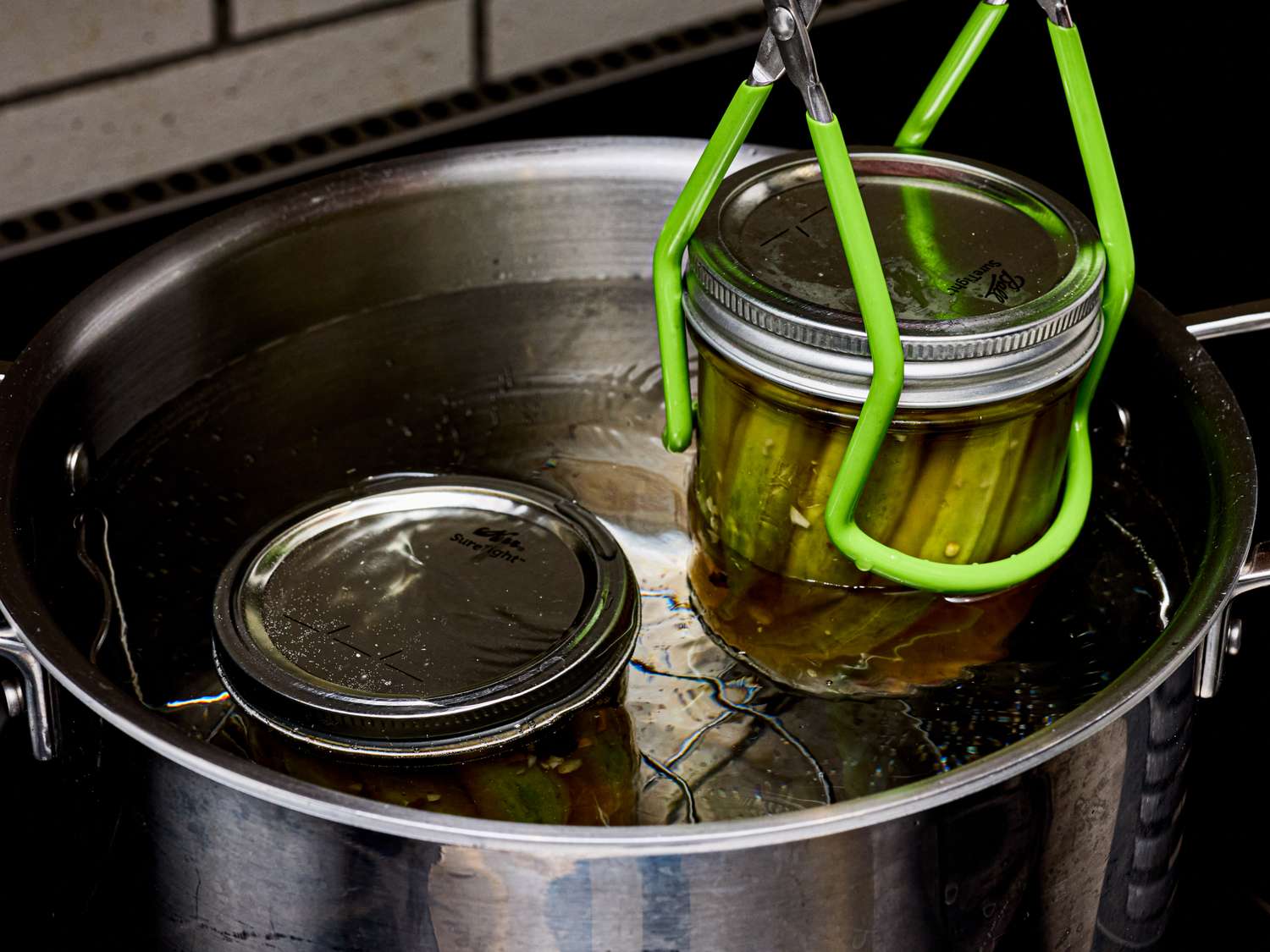 A jar of pickled okra being lifted with tongs from a pot of water during the canning process