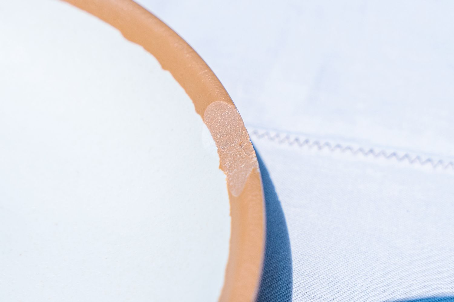 Closeup of Lulu & Georgia Tara Melamine Dinnerware Set ceramic plate with a chipped rim placed on a fabric surface