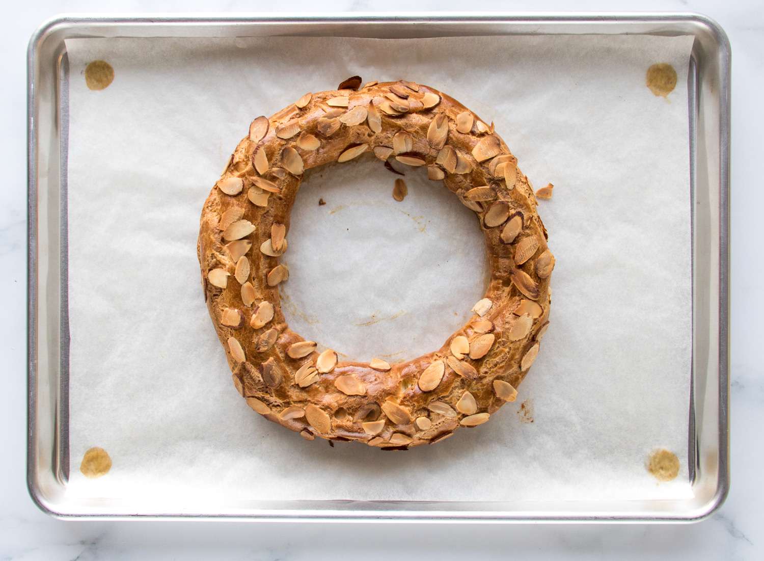 A baked, golden-brown Paris-Brest resting on parchment paper on a baking sheet. 