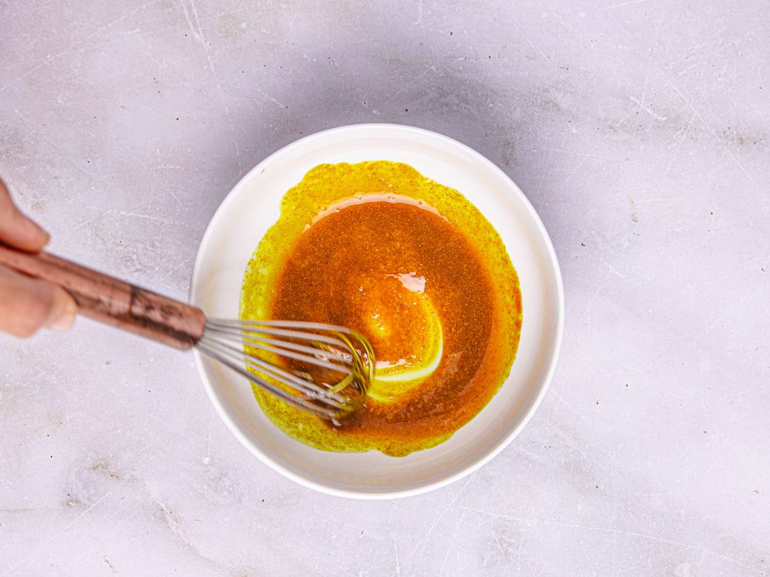 A whisk mixing a sauce in a white bowl on a light surface