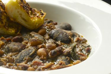 A bowl of ham, bean, and kale stew with two slices of toasted bread on the side. 