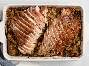 Sliced, herb-roasted turkey breast on top of stuffing inside of a white stoneware baking dish.