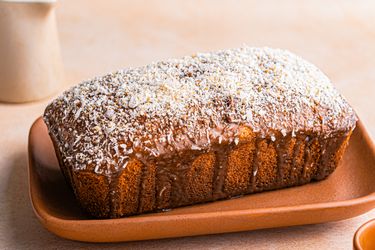 A loaf of banana coconut cake on a platter topped with shredded coconut