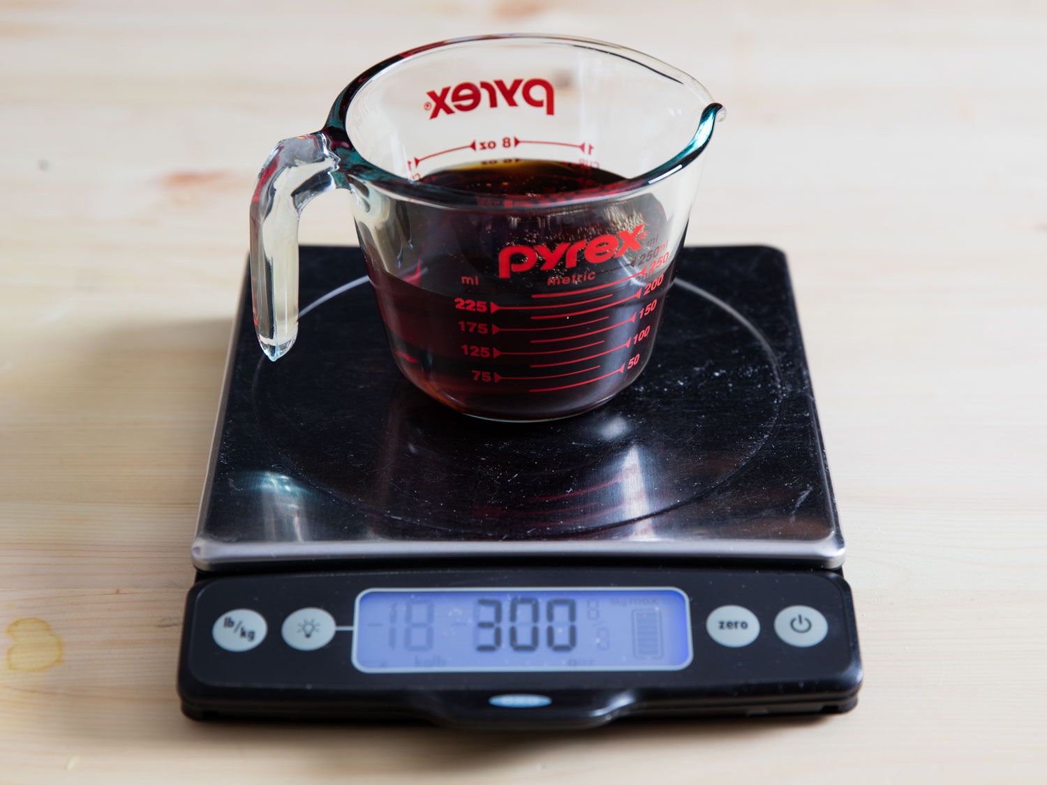 A liquid measuring cup of dark liquid on a digital scale