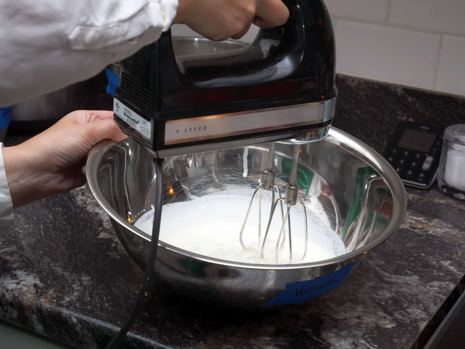 using a hand mixer to whisk whipped cream in a mixing bowl