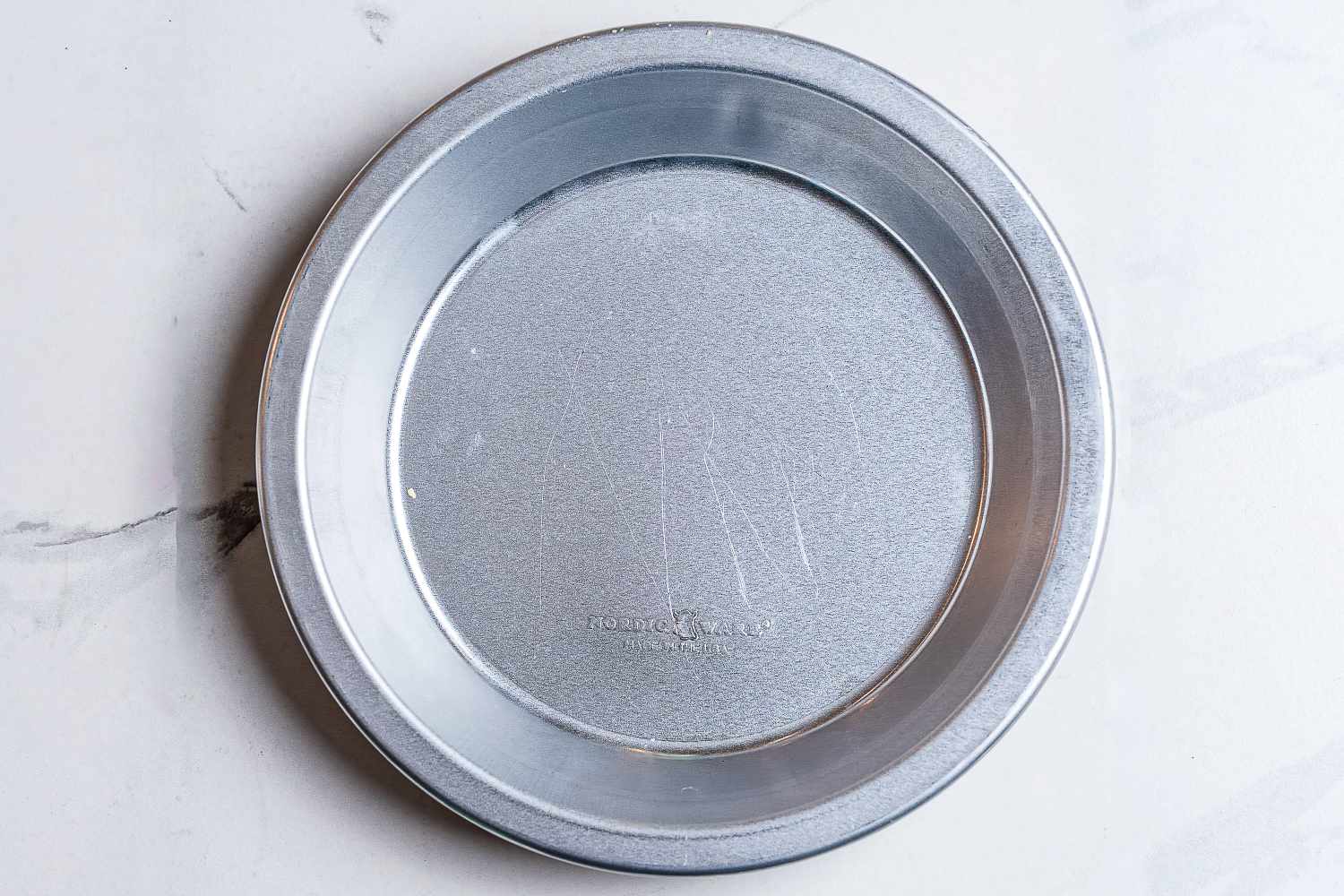An overhead view of a metal pie pan on a marble surface