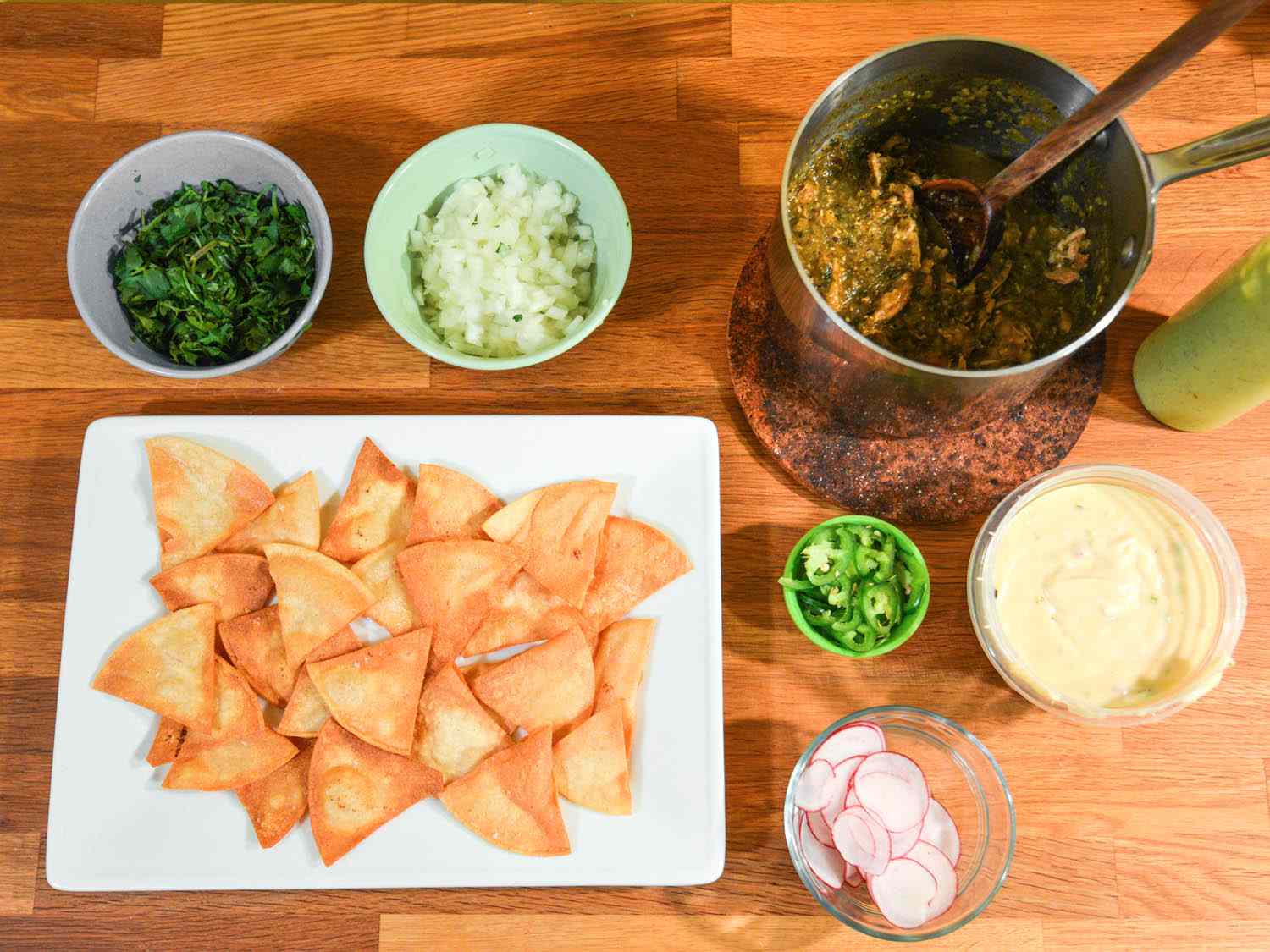 Tortilla chips, chile verde with chicken, cheese sauce, and other toppings displayed in separate vessels