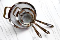 All-Clad Stainless-Steel Strainer, Set of 3 of varying sizes placed on a textured surface