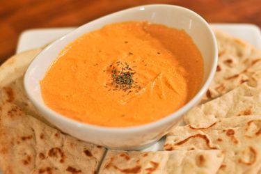 A small bowl of tyrokafteri (hot pepper and cheese dip), served on a platter with wedges of pita bread.