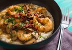 A bowl of shrimp and grits with bacon, chopped herbs, and mushrooms.