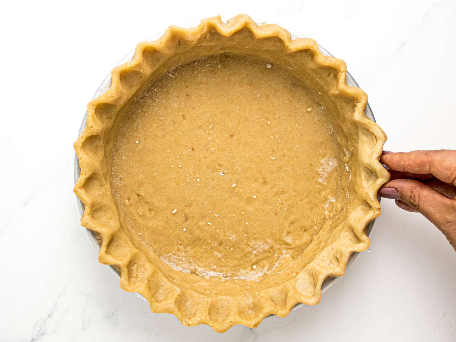A hand holding a pie crust filled with a peanut butter mixture prepared for baking
