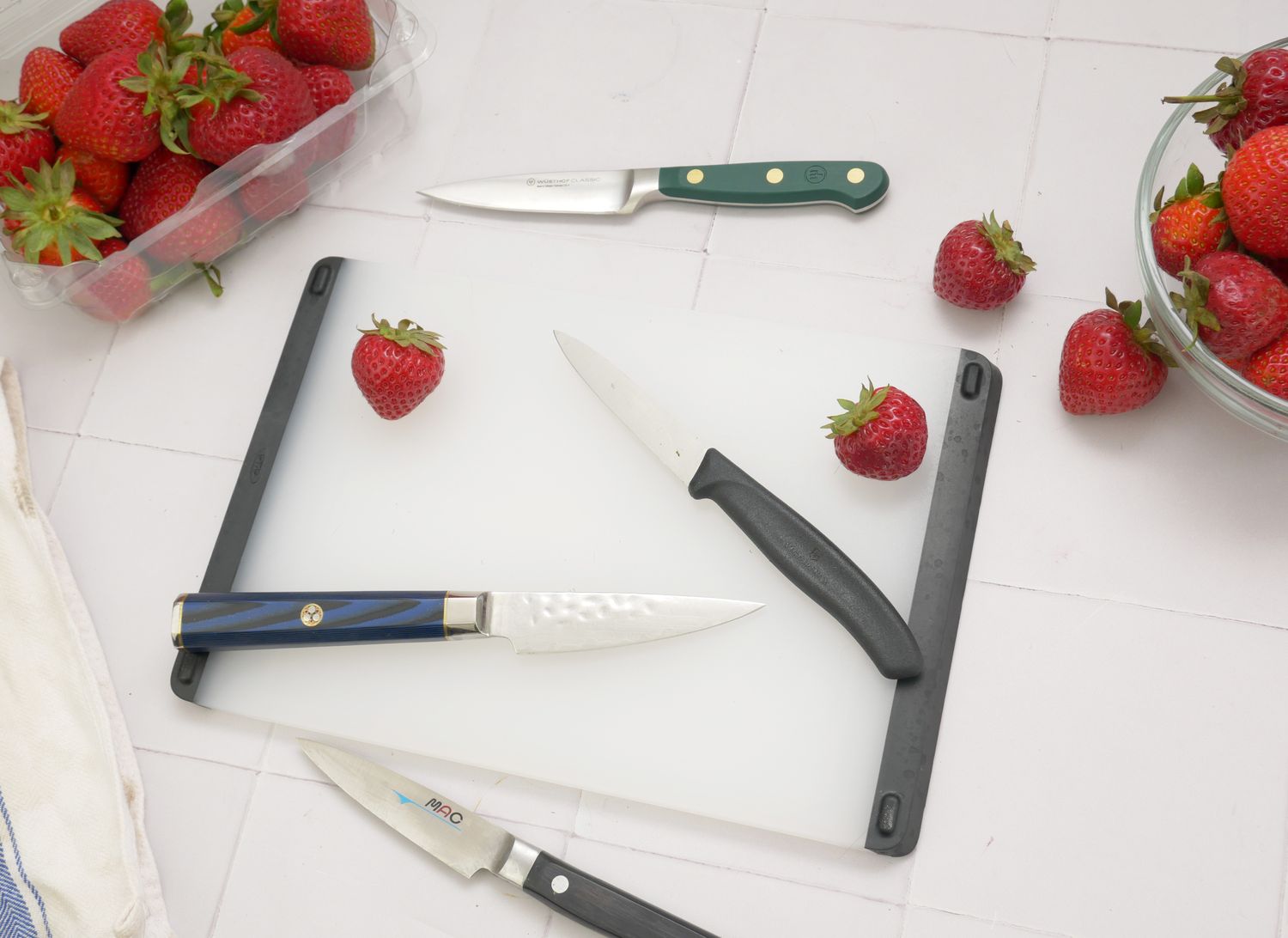 four paring knives on a white tile surface with strawberries
