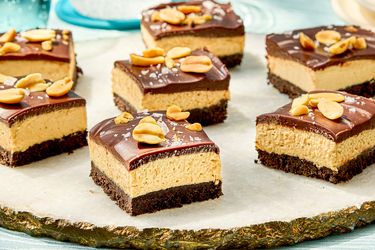 Chocolate peanut butter cheesecake bars garnished with peanuts arranged on a serving plate