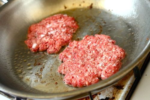 Two ground short rib patties are pan-fried in a skillet.