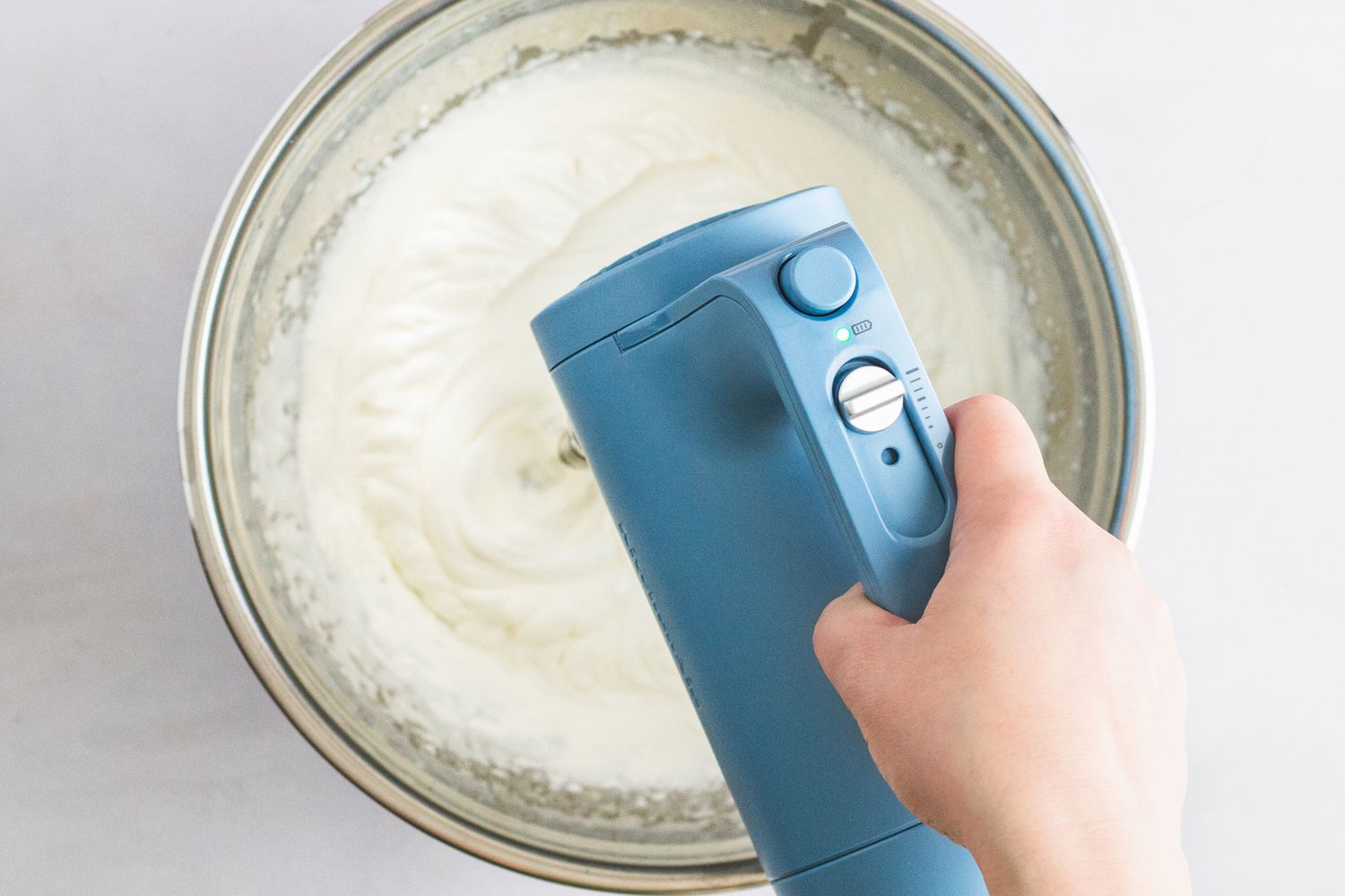 A person using a hand mixer to whip cream.