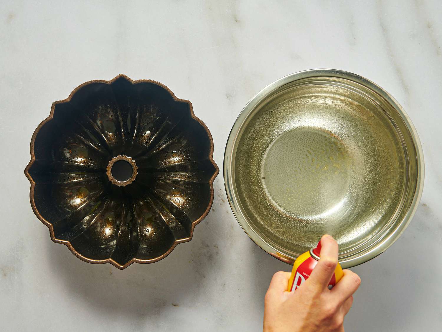 A bundt pan and hand spraying cooking spray into a bowl