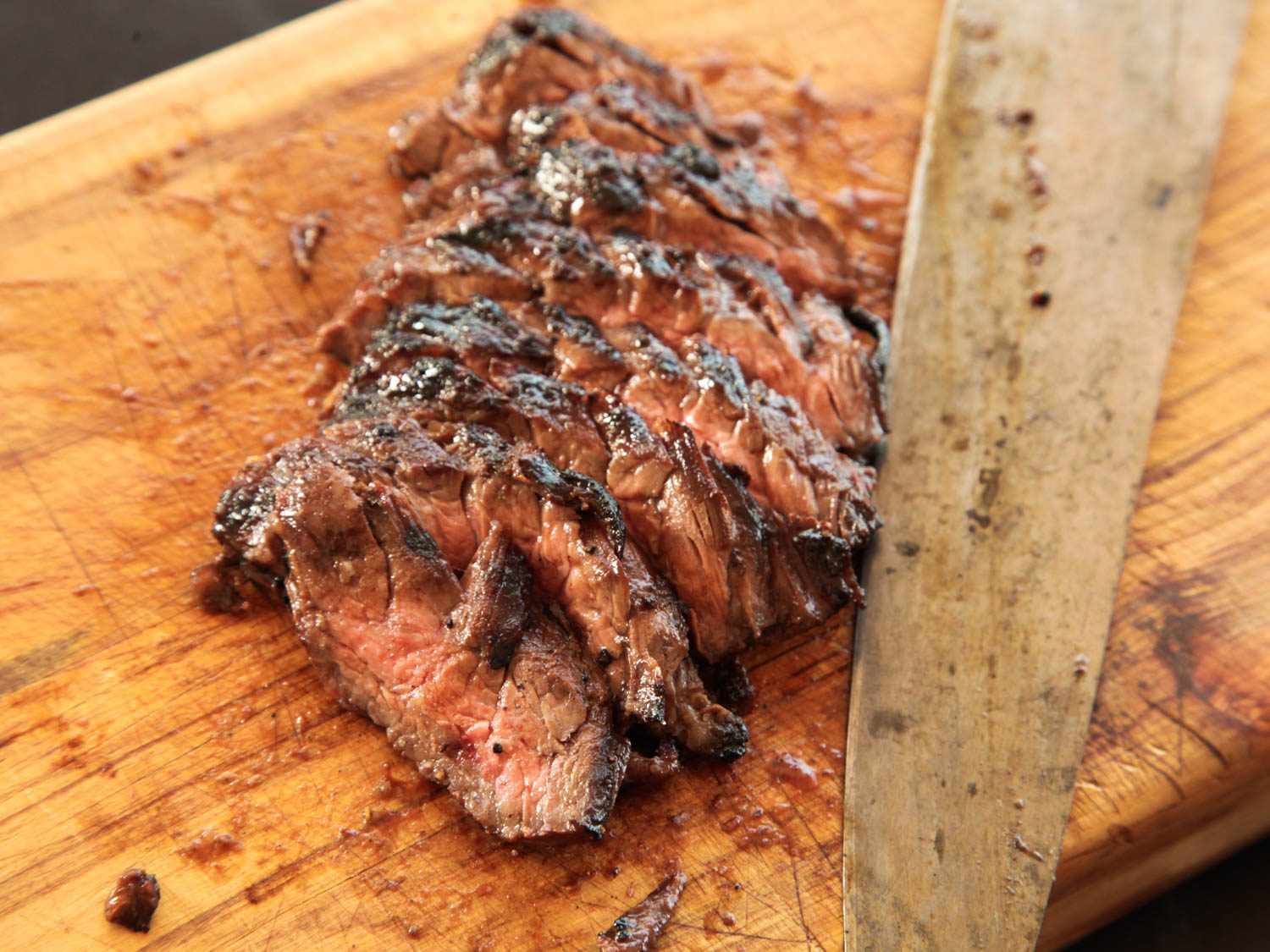 Sliced cooked skirt steak for fajitas slightly fanned out on a wooden cutting board, next to a large knife.