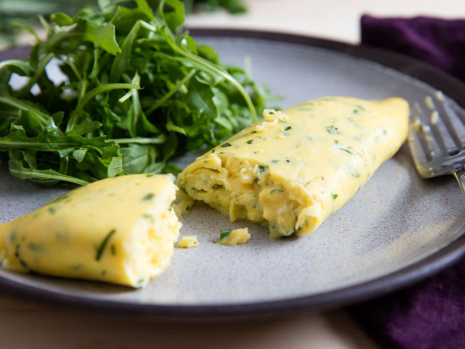 A French omelette with fines herbes, cut open, on a plate with green salad.