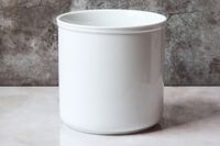 An empty white porcelain utensil crock on a white countertop