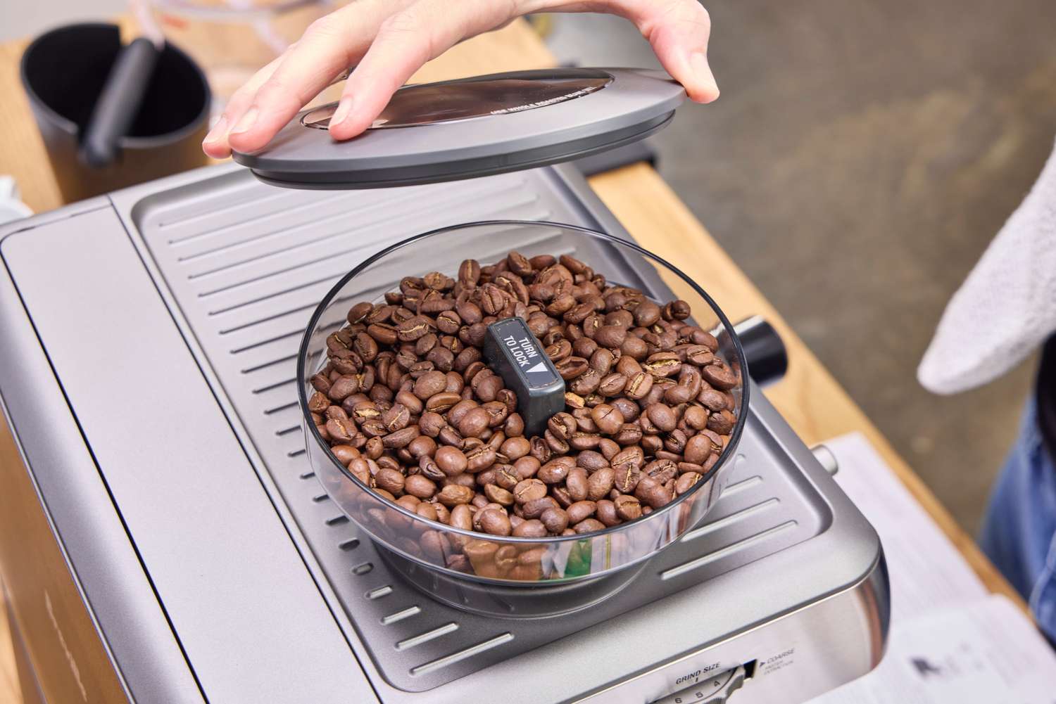A person adds the cover onto the coffee grinder on the Breville The Barista Express Espresso Machine
