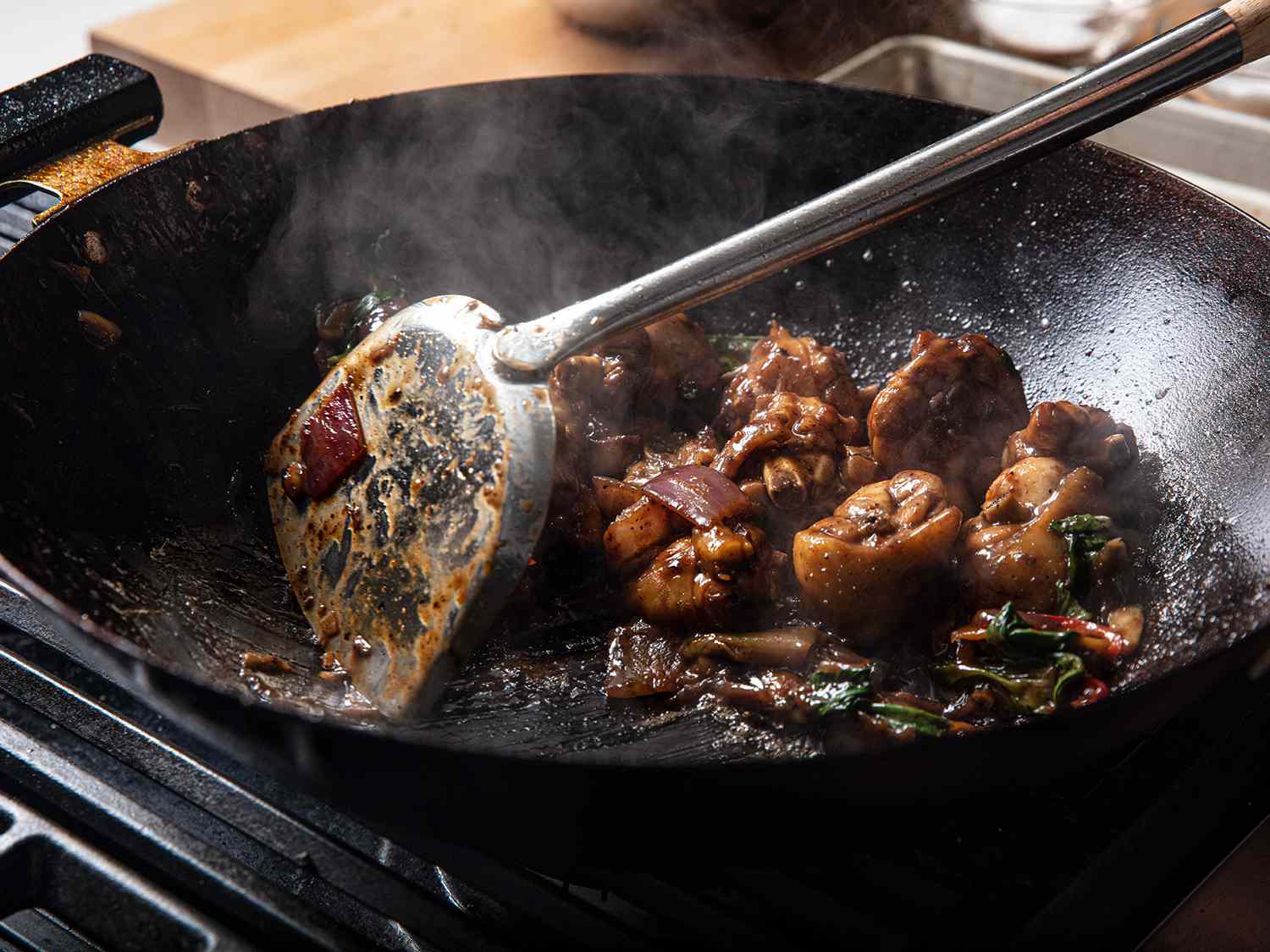 Close up image of a metal spatula moving braised chicken around a wok.