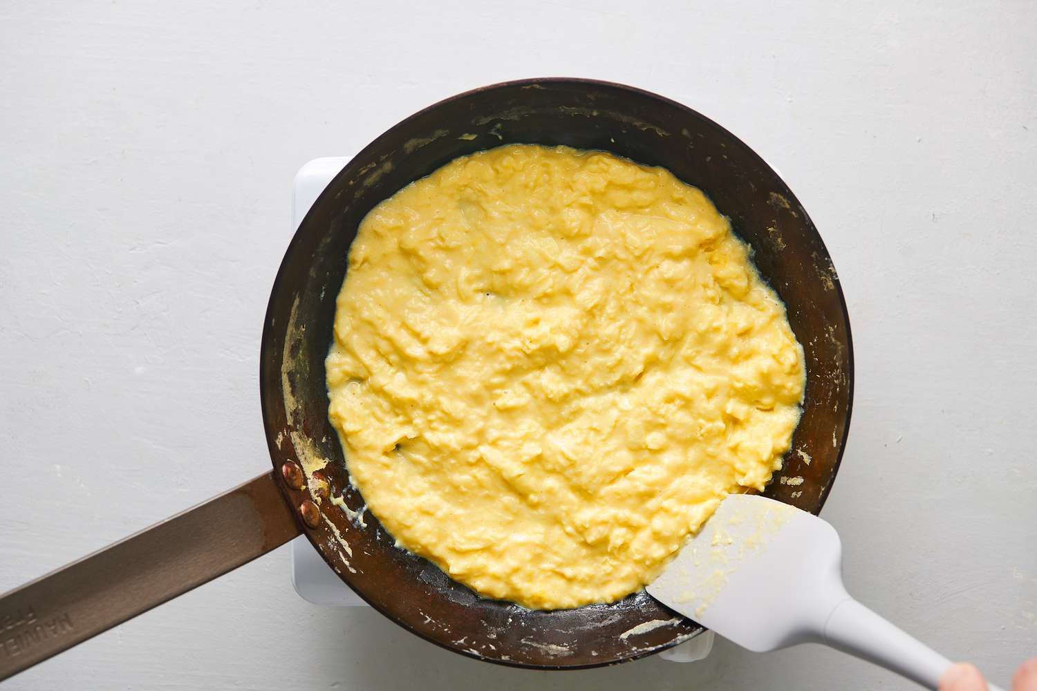 Eggs spread in an even layer around skillet, with any wispy bits scraped down from around the edges