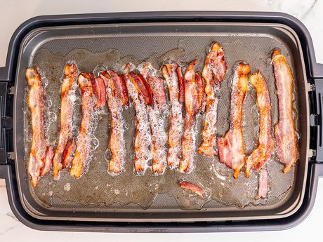 An electric griddle filled with bacon cooking.