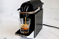 A coffee machine brewing espresso into a clear glass cup
