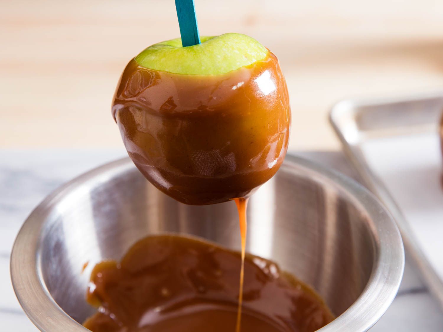 A freshly-dipped caramel apple being lifted from a bowl of caramel.