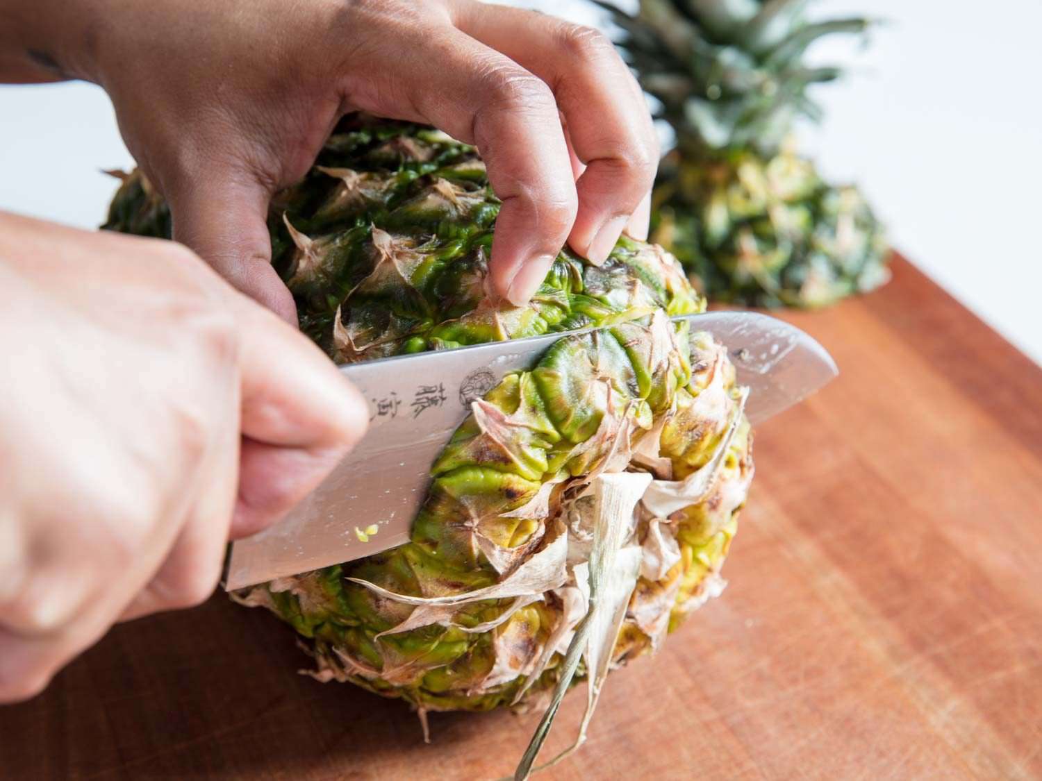 A knife slicing off the bottom of a pineapple