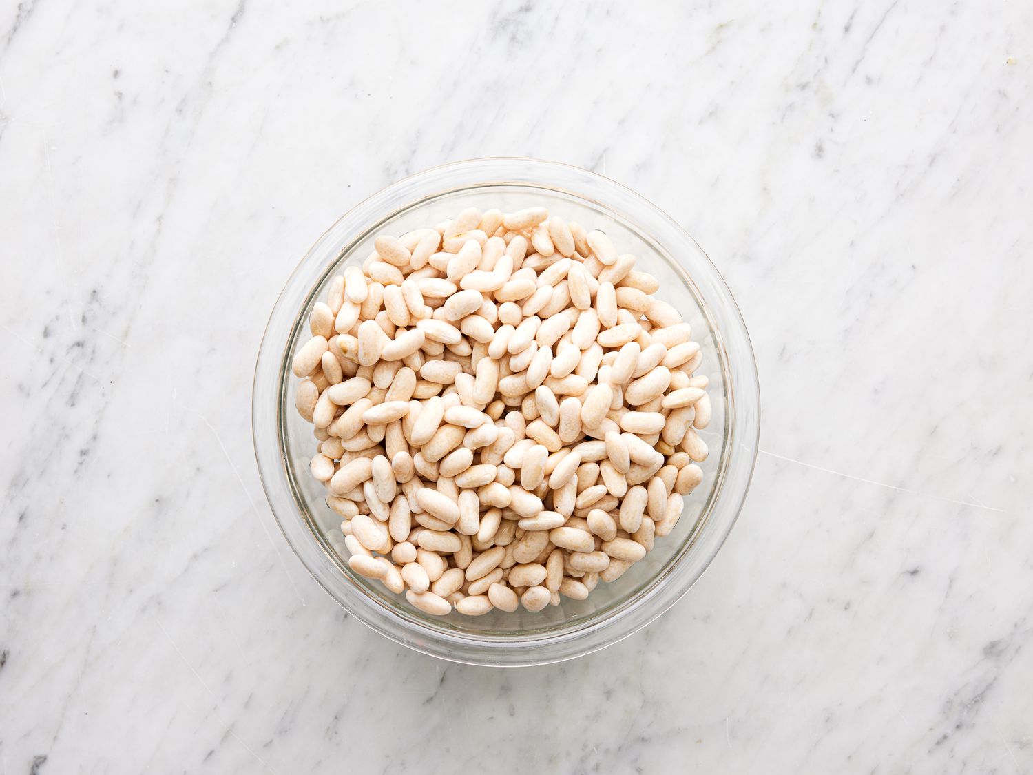 White beans soaking in a bowl on a marble surface.