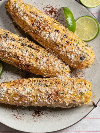 elotes (grilled Mexican street corn) on a plate with limes and chili powder