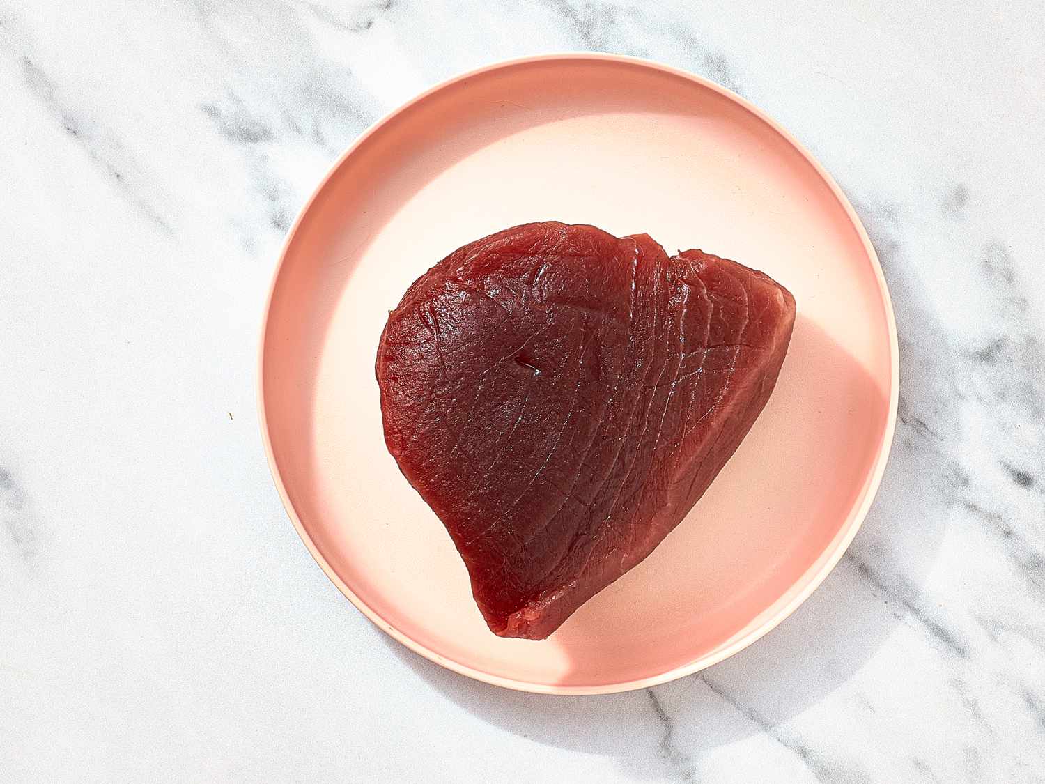 Overhead view of piece of frozen tuna on a pink plate