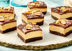 Chocolate peanut butter cheesecake bars garnished with peanuts arranged on a serving plate