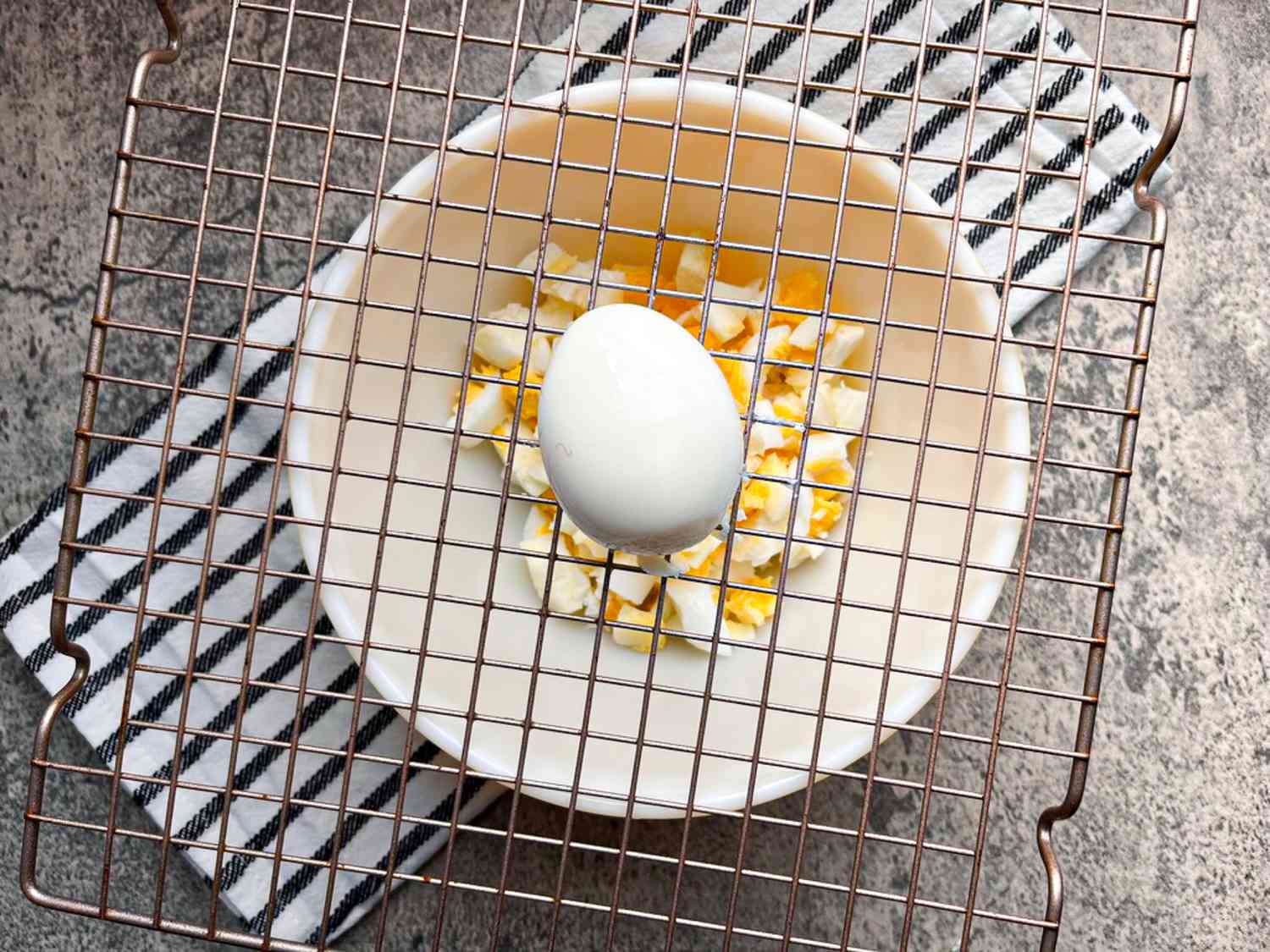 A hard-boiled egg set over a baking rack with a bowl of cubed eggs