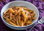 A white shallow bowl of penne boscaiola, or woodsman-style pasta with mushrooms and bacon.