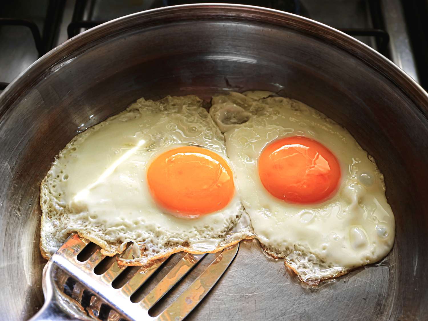 Two fried eggs in a pan with a spatula beneath them