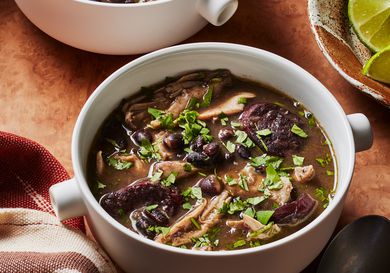 2 mugs of chicken and black bean soup with a bowl of limes on the side. 