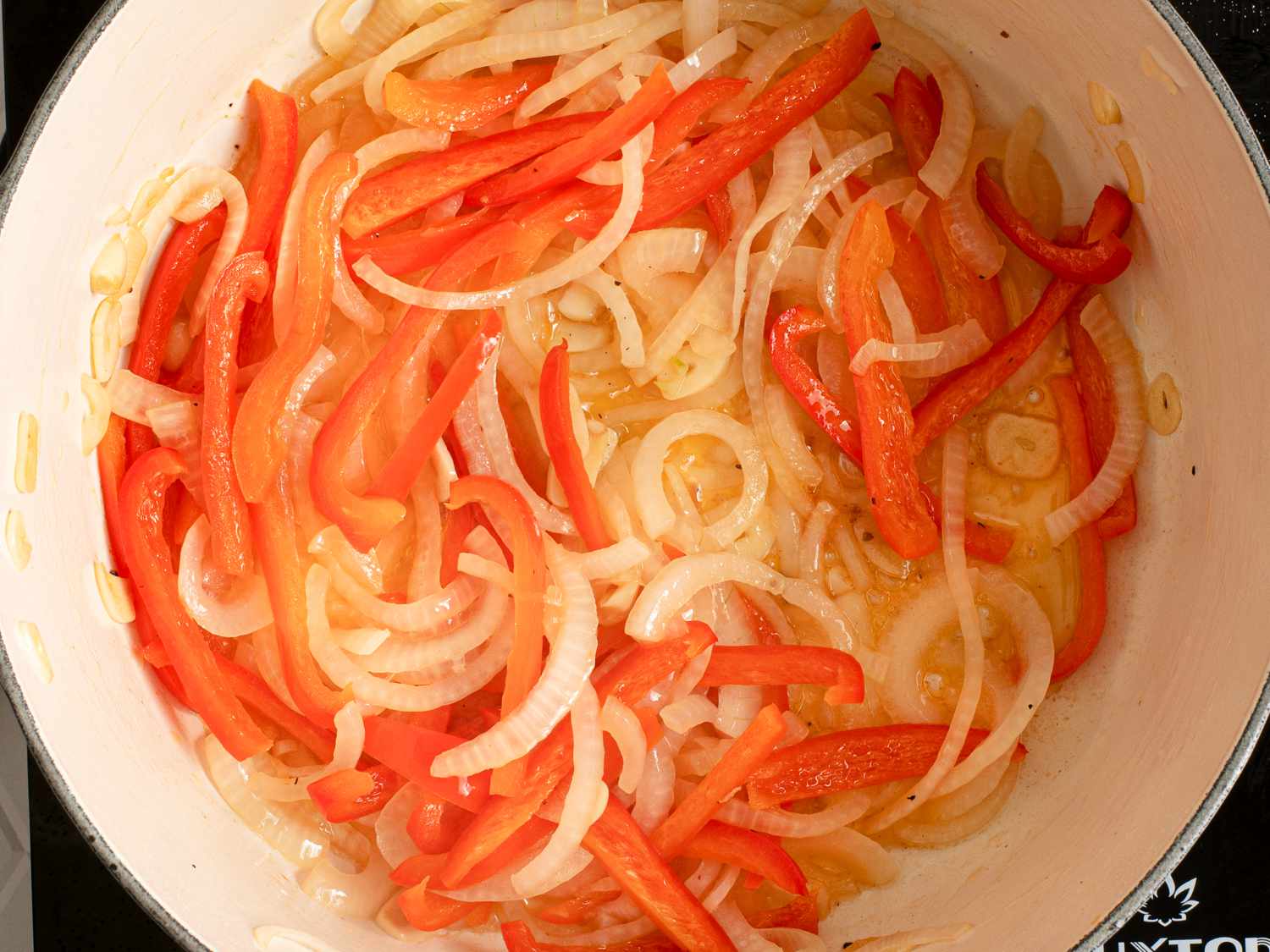 Sliced onions, red peppers, and garlic softening in oil inside of a large Dutch oven.