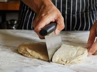A person uses a bench scraper to cut a large piece of dough