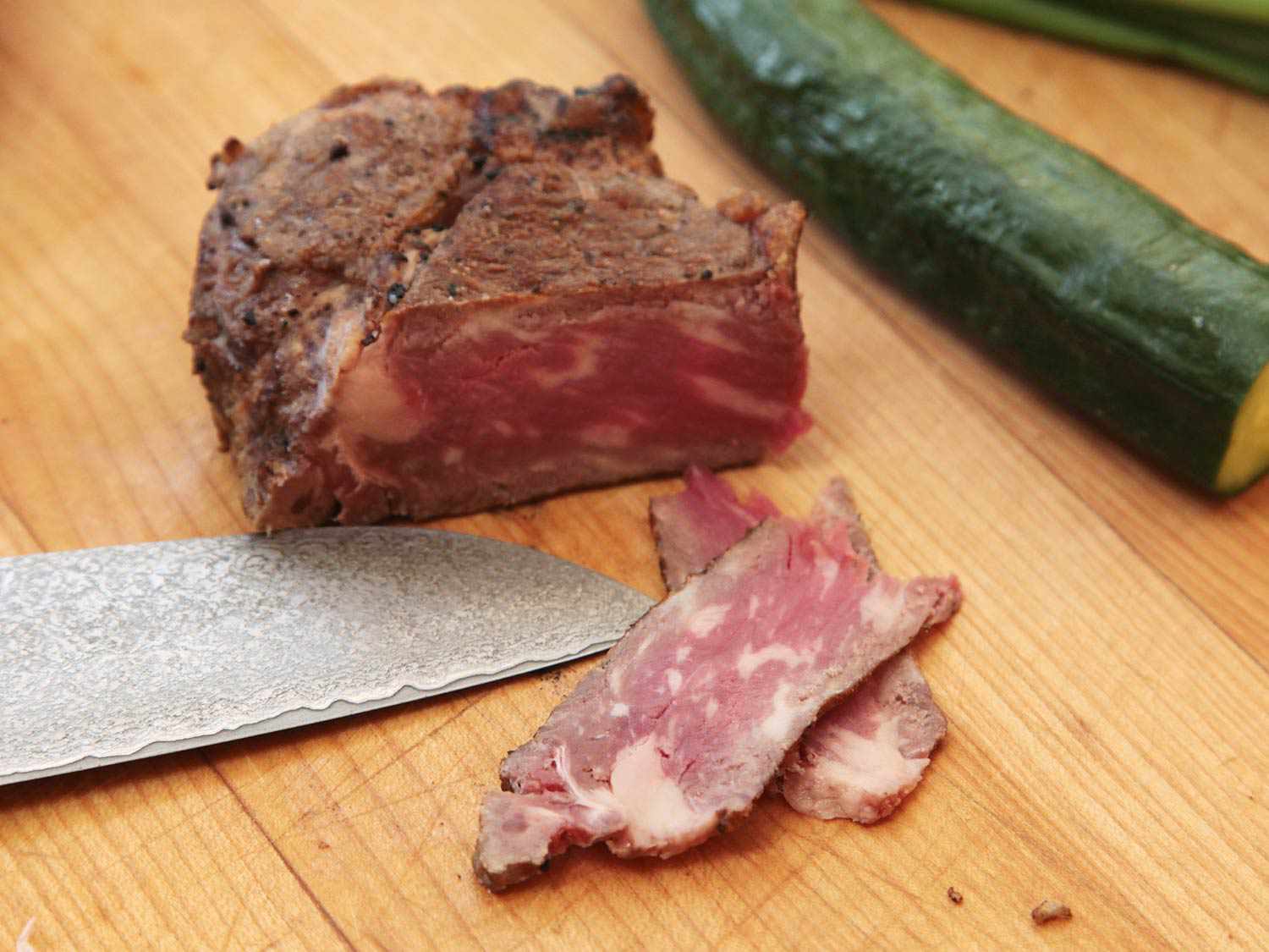 Closeup of a leftover steak being thinly sliced on a cutting board.