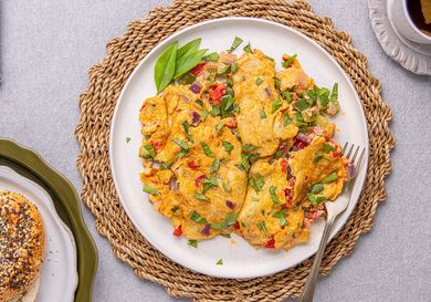 A plate of a prepared Nigerianstyle omelet garnished with herbs accompanied by a bagel and a cup of tea on a woven mat