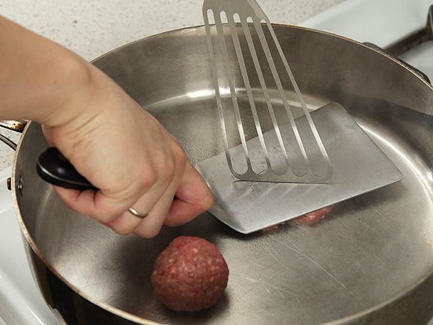 Smashing burger meat with stiff spatula in stainless steel skillet